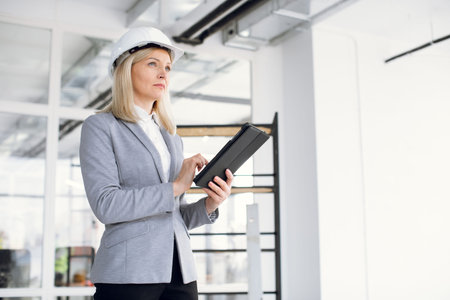 Successful high-skilled focused Caucasian business woman in formal suit and white helmet using...