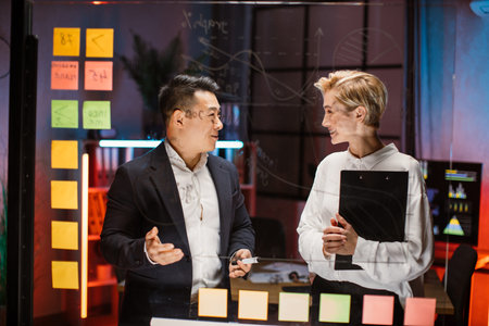 Smiling Asian businessman talking with Caucasian blond female colleague, discussing project strategy...