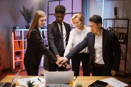 Teamwork, cooperation and support concept. Multiethnic corporate coworkers at the office meeting, standing at the table with modern gadgets and papers and stacking hands togetherの写真素材