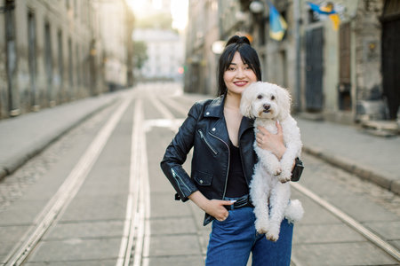 Fashionable brunette Asian woman in jeans coat and black leather jacket, walking in the street...