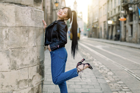 Beautiful young Asian model woman in fashionable casual black leather jacket and denim, and heels,...