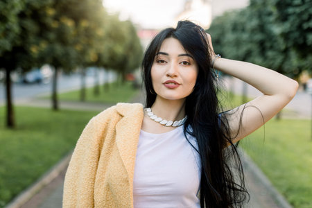 Outdoor close up portrait of young beautiful fashionable Asian brunette lady, wearing stylish...