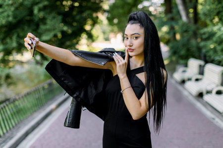 Beautiful sexy mixed raced brunette woman with black ponytail hair, wearing black suit and leather...