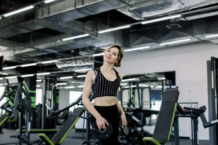 A young Caucasian sportswoman engaged in the gym, doing the exercise of leaning forward with a pancake for the barの写真素材