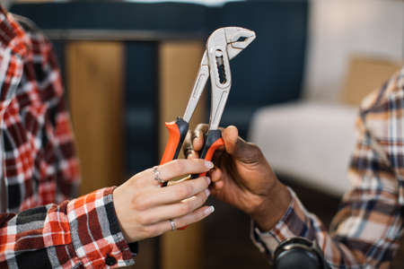 Close up of caucasian woman giving pliers to african american man at living room. Happy wife assisting husband during furniture assembly. Moving concept.の写真素材