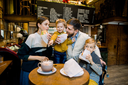 Family having breakfast at city cafe with blurred interior on the background. Adorable children and their parents eating fresh tasty croissants and drinking cocoa drink or coffee.の写真素材