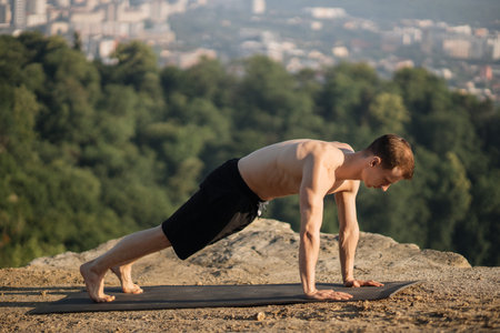 Caucasian athlete with muscular bare torso standing in plank position on yoga mat on fresh air....