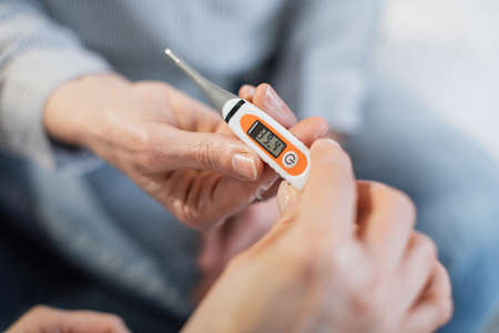 Fever, measuring temperature. Medical examination. Close up shot of unrecognizable doctor and female patient, holding modern thermometer with high body temperature on the screen.の写真素材