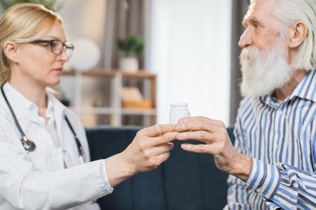 Senior people, geriatric deseases, medication treatment concept. Close up cropped shot of female doctor giving vitamins or medicines bottle to retired man patient, during home medical visit.の写真素材