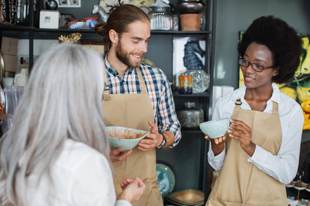 Smiling african woman and caucasian man showing beautiful goods at store to female client....