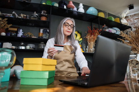 Shopping and discount system concept. Likable grey-haired lady typing on modern laptop while sitting...
