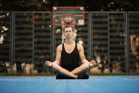 Mental and physical health. Yoga and healthy lifestyle concept. Young sporty man practicing yoga in the city. Handsome muscular man sitting in lotus position.の写真素材