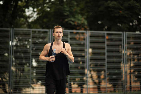 Happy muscular man dressed in sport clothes jogging during morning time at green city outdoor gym. Handsome caucasian guy leading active and healthy lifestyles.の写真素材