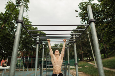 Pull up strength training exercise - fitness man working out his arm muscles on outdoor beach gym...