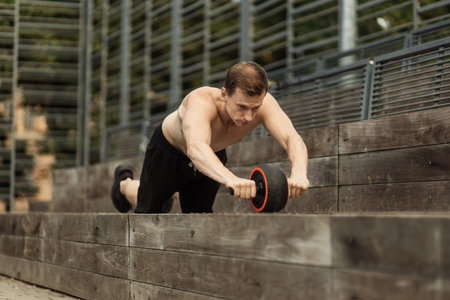 Athletic sporty caucasian shirtless man doing exercise with abs roller wheel to strengthen his...