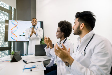 Young African male doctor giving successful speech for medical team, while standing in front of big...
