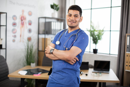 Portrait of young qualified Arabic male doctor smiling and standing with arms crossed at clinic. Healthcare, people and occupations conceptの写真素材