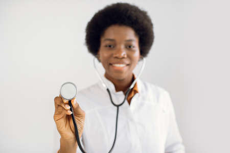 Focus on stethoscope. Blurred close up portrait of happy African American doctor working in hospital, posing with stethoscope. People, occupation, healthcare and medical conceptの写真素材