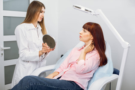 Beautician doctor preparing female patient to skin care procedure in spa salon. Woman cosmetologist is consulting her pretty female client who is looking at mirror and showing her problems on skinの写真素材