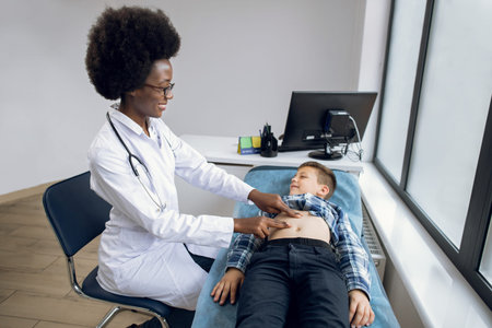 Portrait of smiling joyful African lady doctor performing manual palpation, examining stomach...