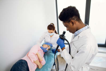 Close up of male Afro-American doctor with an endoscope and female colleague nurse examining young woman patient. Endoscopy, medical examinationの写真素材