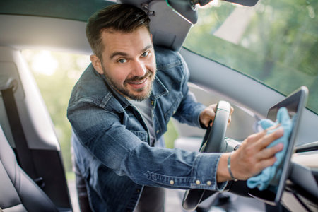 Close up portrait of smiling handsome Caucasian man with beard wiping dust from touchscreen display...