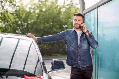 Car celaning and polishing outdoors. Portrait of young Caucasian man standing near his car at self...
