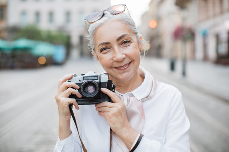 Portrait of charming mature woman posing outdoors with old fashioned photo camera in hands. Old...
