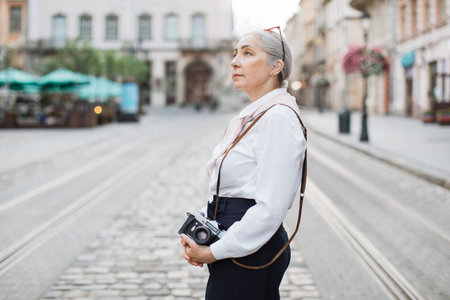 Portrait of charming mature woman posing outdoors with old fashioned photo camera in hands. Old...