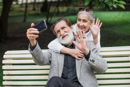 Joyful mature couple using modern smartphone for taking selfie at green park. Retirement with happiness. Concept of technology and family.の写真素材