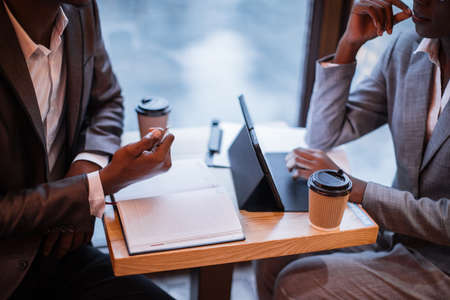Close up of african man and woman using modern tablet and taking notes during working meeting at cafe. Concept of business people and technology.の写真素材