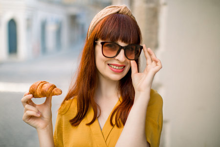 Close up of young attractive woman in stylish yellow clothes, sunglasses and hoop on head, holding...