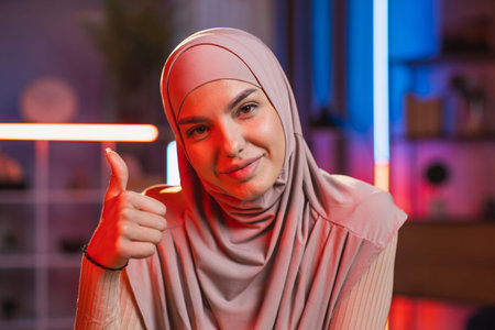 Close up of charming smiling likable young arabian woman in hijab, sitting at the desk at home with...