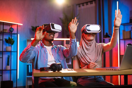 Young multiethnic couple playing games in virtual reality goggles. Black man and muslim woman...