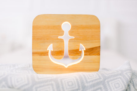 Close up of cozy wooden night lamp with anchor cut out picture, on gray blanket at cozy light...