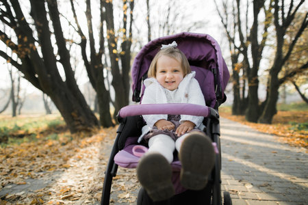 Funny cute little beautiful baby girl, wearing stylish casual warm clothes, sitting in the pink pram...