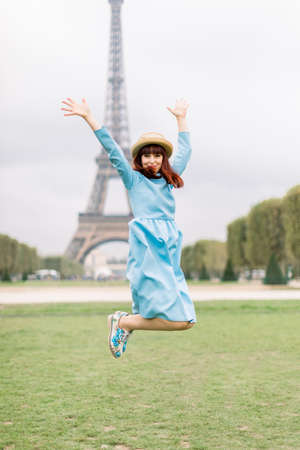 Portrait of pretty fashion young red haired woman in blue dress, having fun and jumping in front of the Eiffel Tower in Paris, Franceの写真素材