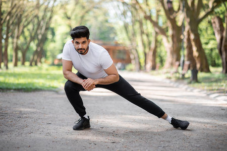 Active male athlete in sport clothes stretching legs before morning run at green park. Handsome...