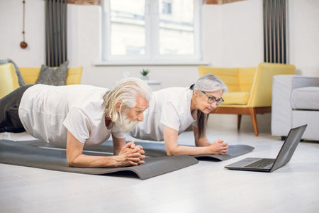 Happy mature couple planking at living room while watching online courses in wireless laptop....