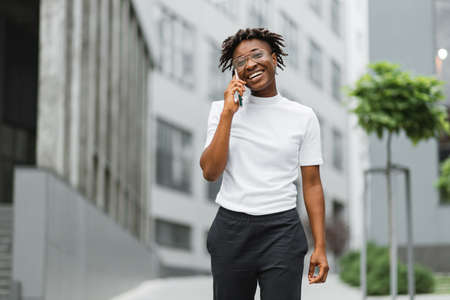 African business woman using smartphone while standing outdoors near office building. Concept of technology, work and modern lifestyles. Successful female career.の写真素材