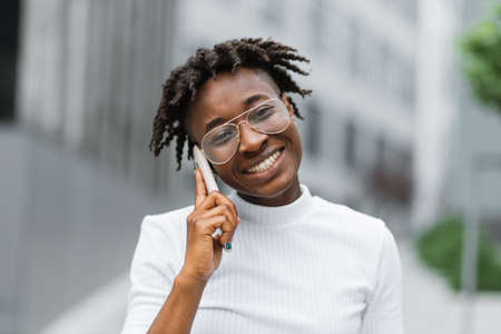 Happy young woman in casual walking while talking over phone. Cheerful african american girl with curly hair using smartphone. Beautiful woman talking on phone outdoor.の写真素材