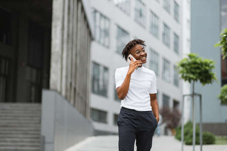 Side view portrait of smiling young african american woman walking and talking with mobile phone outside. Close up portrait of attractive young woman smiling and talking on smartphone.の写真素材