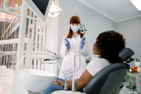 Dental concept. Pretty female dentist in white coat, protective mask and blue latex gloves, shows...