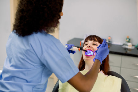 Back angle view of African woman dentist working with dental polymerization lamp in oral cavity of...