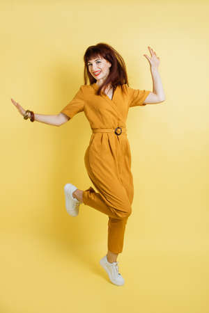 People, emotions, fun and joy. Full length portrait of crazy excited joyful pretty young lady in yellow overalls and sneakers, having fun and jumping on isolated yellow background.の写真素材