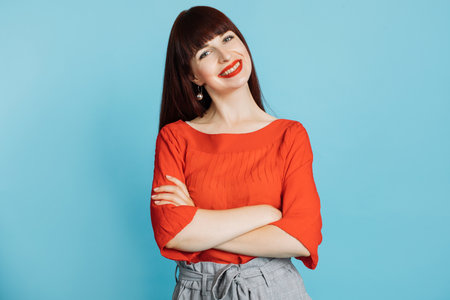 Closeup portrait of confident, successful, pretty young woman in red blouse, posing to camera with arms crossed, isolated on bright blue background. Human emotions, facial expressions.の写真素材
