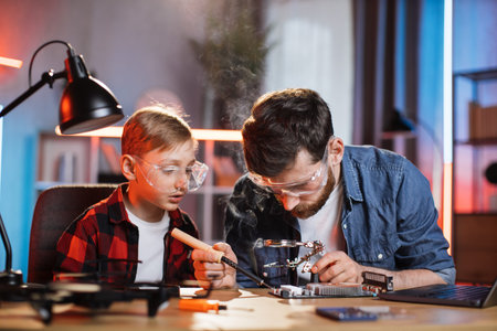 Caucasian father and his son in protective glasses using soldering iron for fixing display card from...