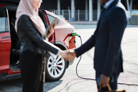 Blur foreground of muslim female dealer handshaking with african male customer outdoor. Red electric car is charging on background. Businessman making expensive purchase.の写真素材