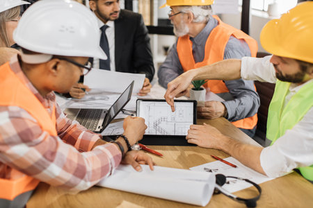 Close up of construction team analysing blueprints during business meeting at office. Multiracial...