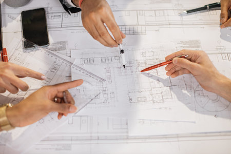 Close up of architects, engineers and designers sitting together at table and analysing blueprints....